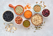 Legumes And Beans Assortment In Different Bowls On Light Stone Background . Top View. Healthy Vegan Protein Food.