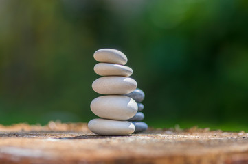 White stones cairn, poise light pebbles on wooden stump in front of green natural background, zen like, harmony and balance