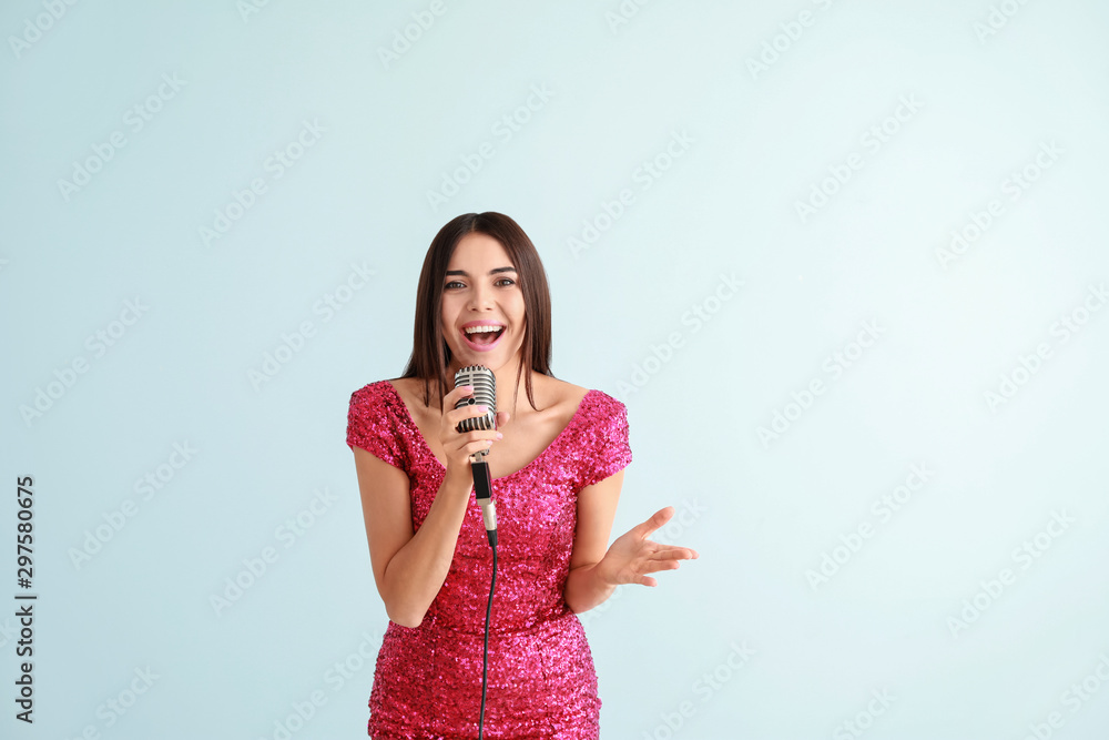 Beautiful young female singer with microphone on light background