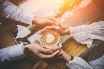 Valentine day, Top view of a young lovers hand holding a heart shaped coffee cup on a wooden table in the coffee shop.