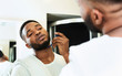 © Prostock-studio - Young black man shaving beard, looking at bathroom mirror