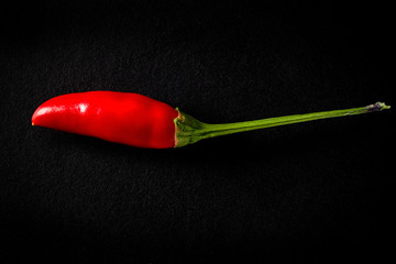 A spicy red pepper resting on a floor, against a black background