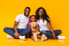 Cute little girl holding teddy bear and posing with parents