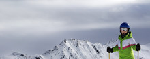 Young Skier With Ski Poles In Sunlight Mountains And Cloudy Gray Sky Before Blizzard