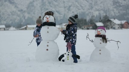 Poster - Family with children, building snowman in the park in little village in Austria, beuatiful landscape scenery