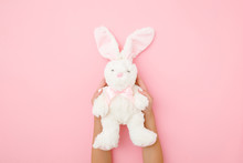 Fluffy White Bunny With Long Ears In Girl Hands On Light Pastel Pink Background. Kids Best Friend. Point Of View Shot. Close Up.