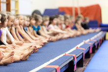Gymnast Girls Sitting In Line On Gymnastic Platform, Unrecognizable Children Barefoot Legs
