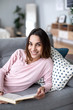 © BestForYou - Woman relaxing on the sofa with a book in her hands while looking up at the camera with a smile.