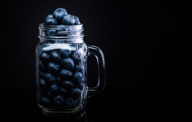 Wall Mural - Blueberries in glass jar isolated on black background.