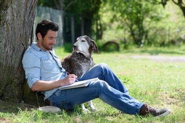 man writing leaning against a tree with his dog