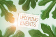 © Artur - Writing note showing Upcoming Events. Business concept for the approaching planned public or social occasions Leaves surrounding notepaper above empty soft pastel table