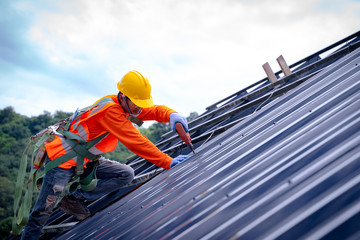 Poster - Roofer worker in protective uniform wear and gloves, using air or pneumatic nail gun and installing asphalt shingle on top of the new roof,Concept of residential building under construction.