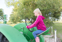 Close Up Of A Little Girl Sitting On A Tractor Seat With Hands On The Steering Wheel
