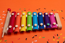 Wooden Xylophone In Rainbow Colors For Children An Isolated On Orange. Paper Colorful Musical Notes Surrounding