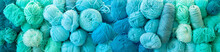 Yarn Of Green, Turquoise, Aquamarine And Blue Colors. White Wood Background. Knitting Needles And Crochet Hooks. Scissors. Long Background.