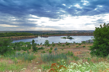 Scenic view on flooded quarry with blue water under cloudy sky with green fields and trees around it. An industrial facility that has become a landmark and place of rest. Zugres,Donetsk region,Ukraine