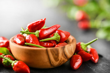 Wall Mural - Hot spice peppers in wooden bowl. Chili pepper on dark stone table or black background.