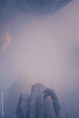 Fotomural Looking up on small christian church among modern high multi-levels residential buildings
