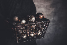 Wire Basket Full Of Christmas Or New Year Tree Golden Vintage Decoration Toys In Hands Of Lady In A Gray Warm Sweater, Selective Focus, Square Crop