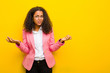 © kues1 - black business woman feeling clueless and confused, not sure which choice or option to pick, wondering against orange wall