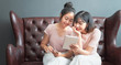 © sutthinon602 - Young asian women happy couple sitting on sofa shopping online using laptop a computer and smartphone in living room at home. Two young friends watching a video on a tablet in the living room.