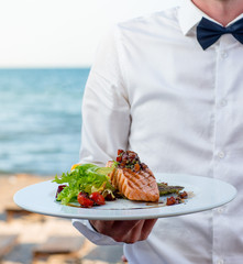 Wall Mural - waiter holds a plate of grilled smoked salmon with lettuce, tomato, pepper