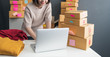 © sutthinon602 - Young business woman working selling online. Entrepreneur owner using Laptop or tablet taking receive and checking online purchase shopping order to preparing pack product box. Online shopping