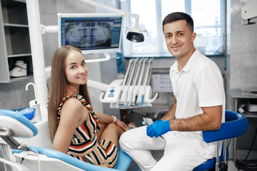 Dental clinic. Reception, examination of the patient. Teeth care. Young woman undergoes a dental examination by a dentist.Happy patient and dentist concept.Male dentist in dental office talking with g