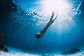 Wall Mural - Attractive woman free diver glides with fins over sandy sea. Freediving in a tropical ocean