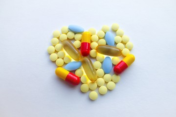 A lot of colorful tablets are laid out in the form of a heart on the background of a white textured rough sheet of paper with space for text