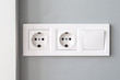 © MariiaDemchenko - A closeup view of a group of white european electrical outlets and a switch located on a gray wall