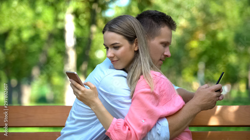 Cuadros en Lienzo Young couple hugging at park chatting on smartphones, lack of communication
