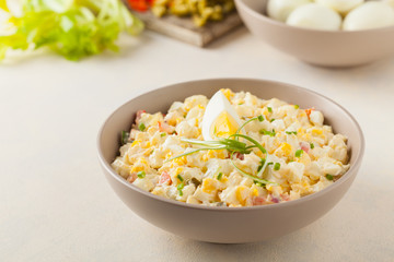 A light egg salad with celery, gherkin, pepper and mayonnaise. Served in a bowl on a light background. Front view.