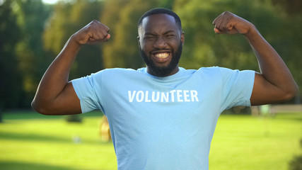 Excited african male volunteer t-shirt showing strength gesture, donation unity