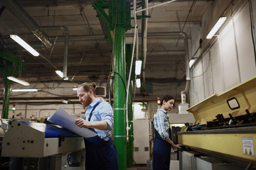 Two manual workers in overalls busy with their work on lathes in printing plant