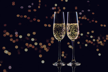 Two glasses of champagne on black background with golden bokeh.