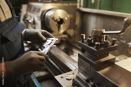 Fotomural Close-up of manual worker in protective gloves measuring metal detail with speci
