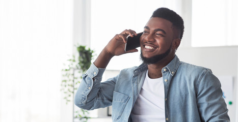 Wall Mural - Cheerful african american guy talking on cellphone indoors