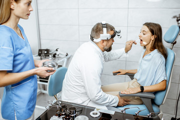 Wall Mural - Patient with senior otolaryngologist and assistant in ENT office during a medical examination, doctor examining throat