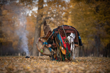 Wall Mural - Mongolian traditional shaman performing a traditional shamanistic ritual with a drum and smoke in a forest during autumn afternoon. Ulaanbaatar, Mongolia.