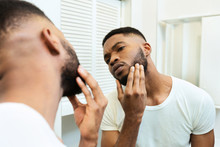 Concentrated African Guy Looking At His Beard At Bathroom Mirror
