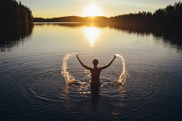 young woman splashing in the lake at sunset after sauna in finland