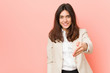 © Asier - Young brunette business woman against a pink background stretching hand at camera in greeting gesture.