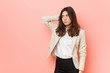 © Asier - Young brunette business woman against a pink background touching back of head, thinking and making a choice.
