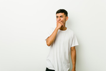 Wall Mural - Young hispanic man thoughtful looking to a copy space covering mouth with hand.