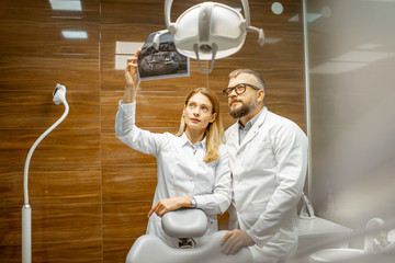 Wall Mural - Two experienced dentists examining x-ray of a human jaw at the dental office