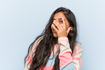 Wall Mural - Young fashion indian woman blink at the camera through fingers, embarrassed covering face.