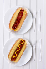 Top View Of An All White Place Setting With Hot Dogs One With Ketchup, One With Mustard.