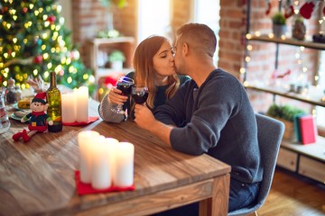 Young beautiful couple smiling happy and confident. Toasting with cup of wine and kissing celebrating christmas at home