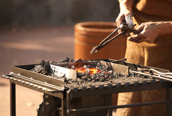 Blacksmiths forge horseshoes. Heated metal for forging according to the ancient method. An old blast furnace. Workshop horse harness manufacturing forged implements. Masters at the Fire Furnace